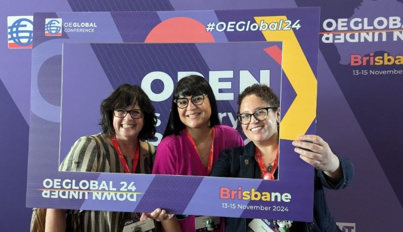 from left to right, photo of Kathy Essmiller, Liliana Diaz, and Heather Blicher in front of the purple media wall at the OEGlobal24 Conference in Brisbane 13-15 November 2024