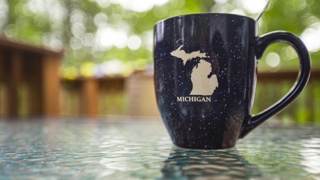 A dark blue mug with a Michigan silhouette on a glass table, with a blurred outdoor background. by robinsonk26 from Pixabay